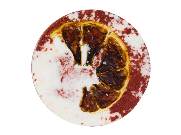 circular half red and white blood spatter appearance bath bomb with a blood orange pressed on top