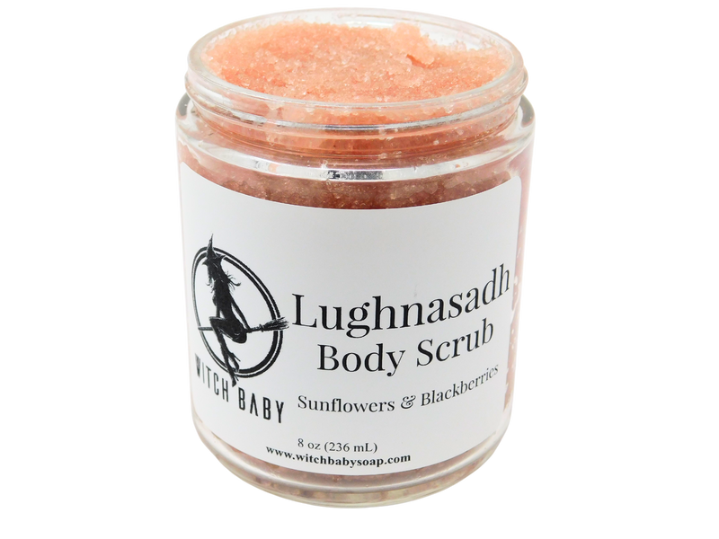 8 oz glass jar of light pink sugar scrub with white label that reads: Lughnasadh Body Scrub. Sunflowers & Blackberries.