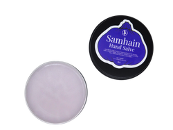 purple hand salve packaged in a 2 oz black tin with the lid removed to show the product. lid has a purple pumpkin shaped label that says Samhain Hand Salve with the product listed beneath it. 