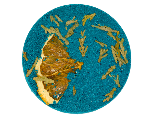 green circular bath bomb pressed with orange peel and cedar